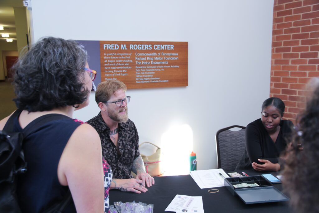 Arno a blond white man with glasses at a table talking to the black woman next to him