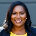 Dr. Jamilia Blake head shot, a Black woman with medium length dark hair wearing a black blazer and bright yellow top