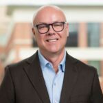 Jim Link headshot, a bald white man wearing eye glasses, a brown suit coat and a blue shirt